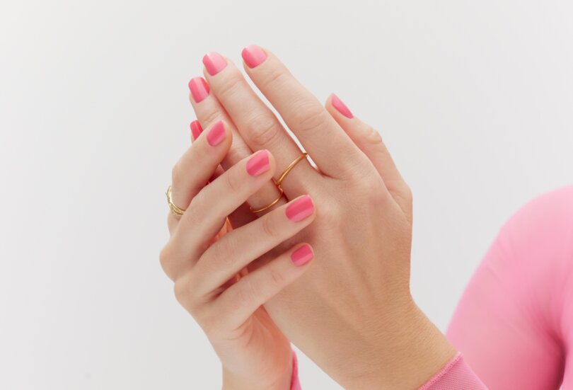 Nahaufnahme von zwei schönen Händen einer jungen Frau mit pink lackierten Nägeln als Sinnbild für den Make-up Trend Bright Nails im Frühling Sommer 2024