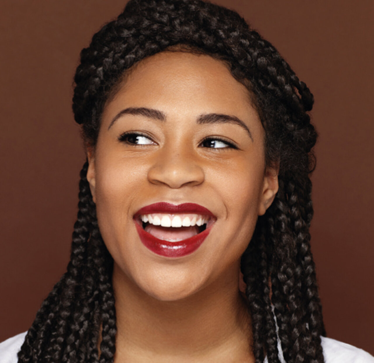 Portrait einer jungen Frau mit dunklem Hauttyp, die fröhlich lacht und einen beerenroten Lippenstift trägt