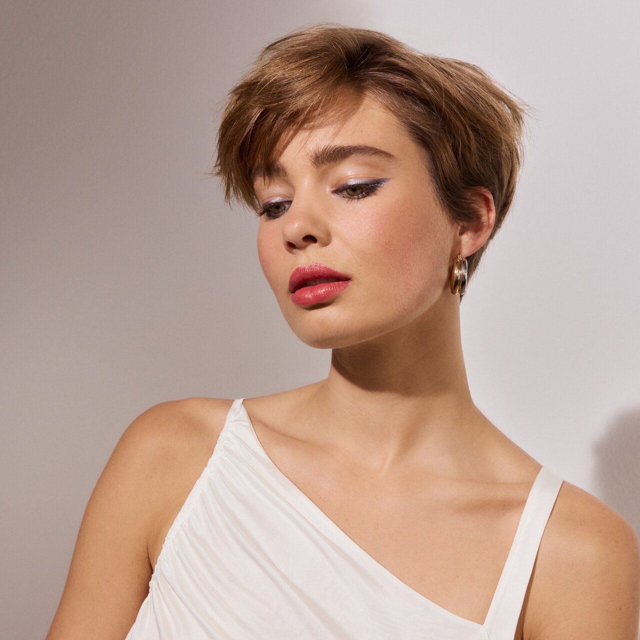 Frau mit kurzen braunen Haaren hat die Augen leicht geschlossen, um ihren leicht metallischen Lidstrich als Augenmakeup-Trend 2026 Luminous Line zu präsentieren 