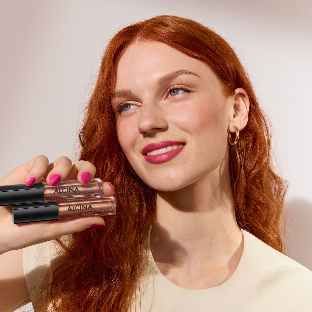 Frau mit langen rötlichen Haaren hält Glow Fluid in der Hand, das als Lidschatten, Highlighter und Bronzer eingesetzt werden kann als Sinnbild für den Augenmakeup-Trend 2026 Timeless Luxury 