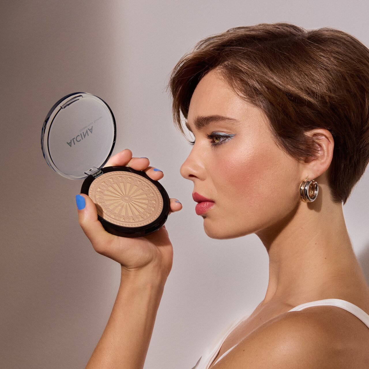 Frau mit kurzen Haaren hält einen goldfarbenen Bronzer in geöffneter Dose in der Hand als Sinnbild für den Make-up Trend 2026 Golden Hour Look 
