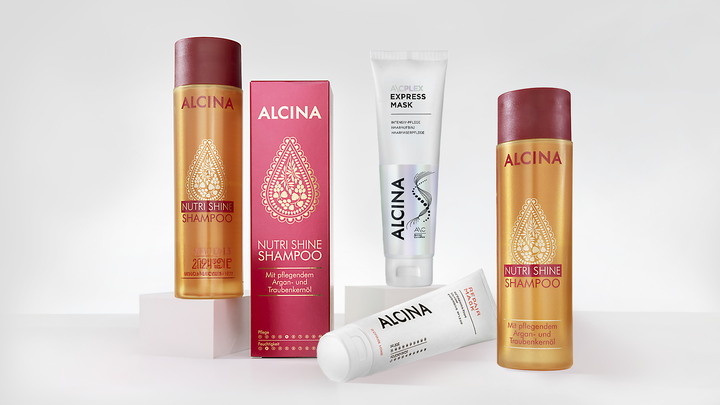 ALCINA Haarpflegeprodukte auf weißen Podesten: eine Express-Maske, eine weiße Tube und zwei goldene Nutri-Shine-Shampoos.