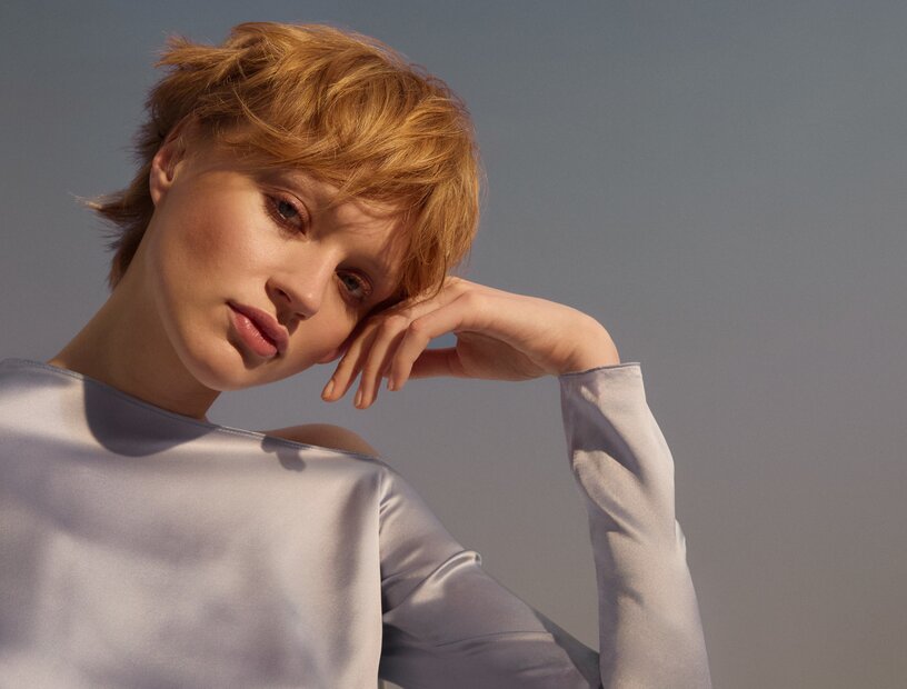 Die Styles der ALCINA Kollektion Golden Veil sind inspiriert von der Goldenen Stunde, der magischen Phase zwischen Tag und Nacht. Porträt einer schönen jungen Frau mit einem honigblonden Pixie-Kurzhaarschnitt