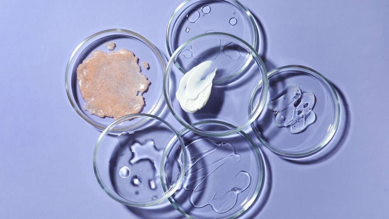 Retinol-Creme pflegt die Gesichtshaut zart und macht sie ebenmäßig Verschiedene Kosmetik-Wirkstoffe in sechs Petrischalen auf violettem Hintergrund als Sinnbild für Vitamin A und Retinol in der Hautpflege