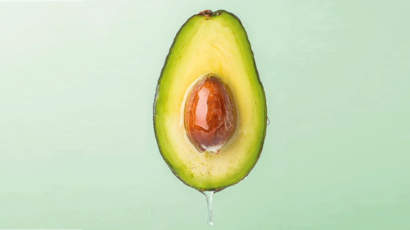 Die hoch entwickelte Emulsions-Galenik mit Avocadoöl bildet die Grundlage der ALCINA Haarfarben. Längs halbierte Avocado mit gelb-grünem Fruchtfleisch und ganzem Avocadokern in der Mitte, von dem Öl herunter tropft.