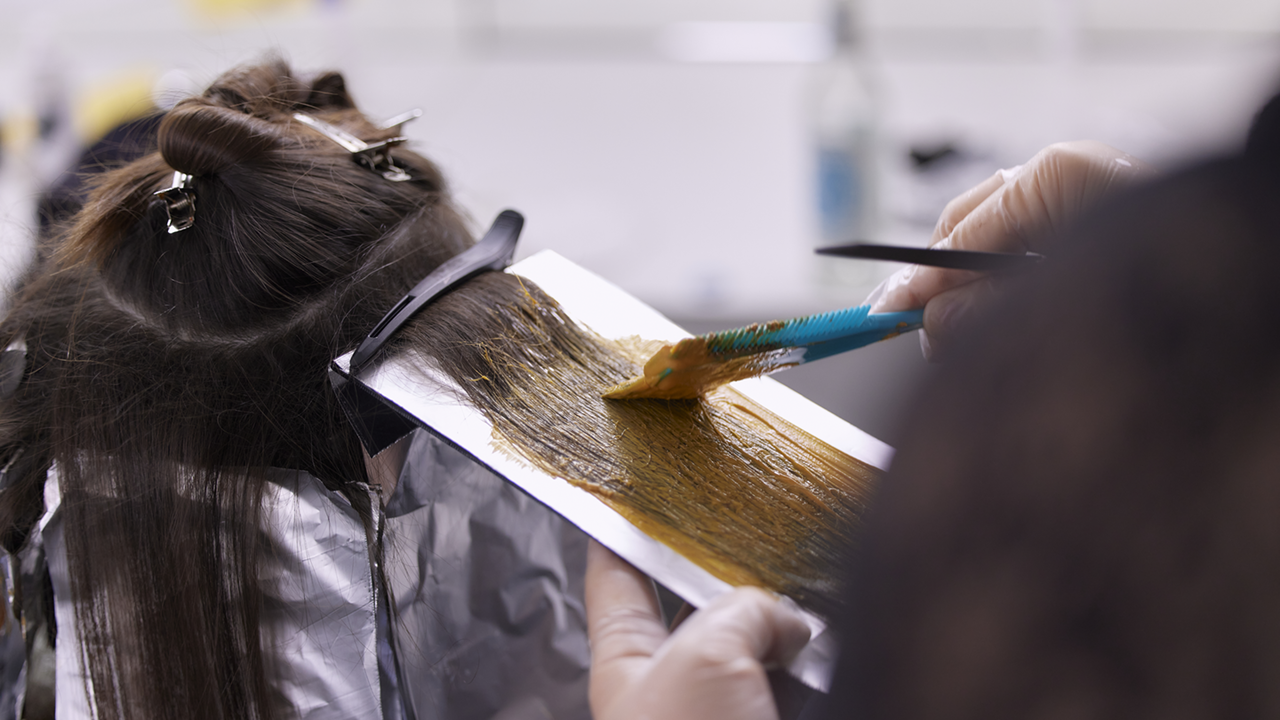 Rückansicht einer Frau, bei der gerade die Ombre und Balayage Haarfärbetechnik mittels Pinsel-Farbauftrag und Folientechnik durchgeführt wird