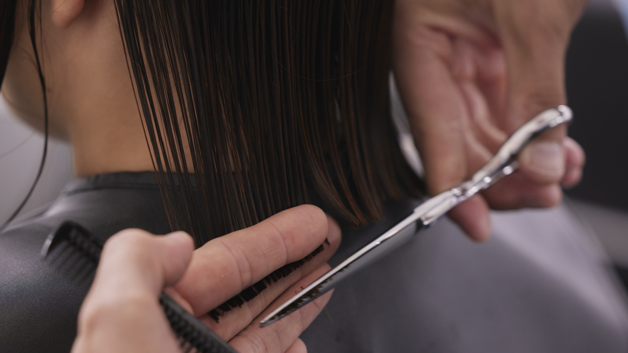 Abhilfe bei Spliss: Spitzen schneiden beim Friseur Friseur schneidet die Spitzen einer Kundin mit einem schulterlangen Bob, um Spliss zu entfernen
