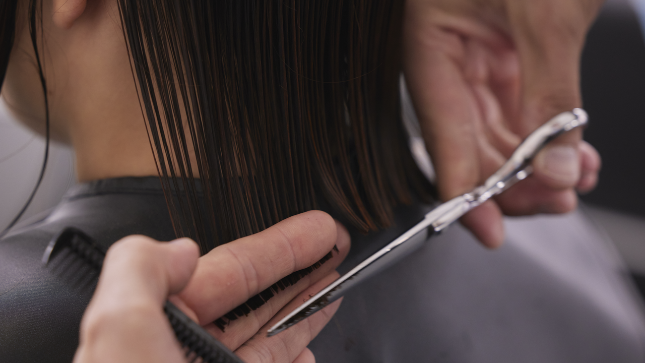 Friseur schneidet die Spitzen einer Kundin mit einem schulterlangen Bob, um Spliss zu entfernen 