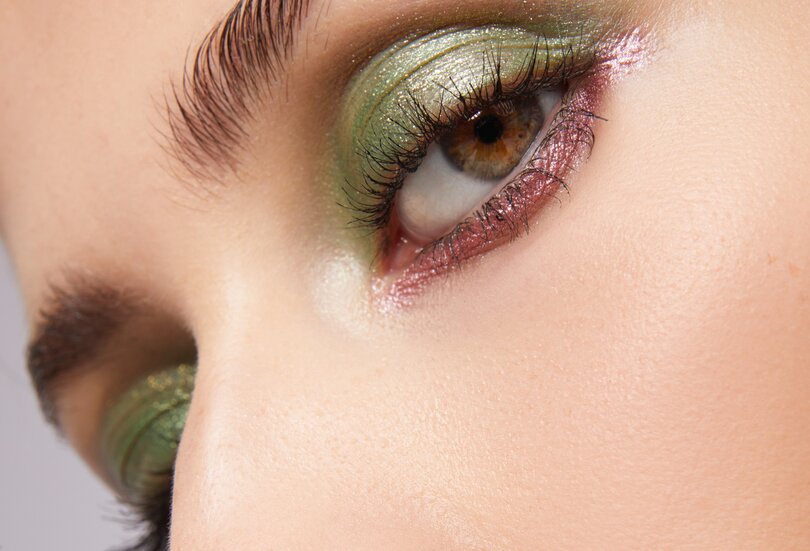 Komplementärfarben sind ein besonderer Hingucker für den großen Auftritt Nahaufnahme einer schönen jungen Frau mit stark geschminkten Augen mit grünem und rosa Lidschatten und Metallic Effekt als Sinnbild für den Make-up-Trend Metallic Glamour als Color Blocking im Herbst Winter 2023