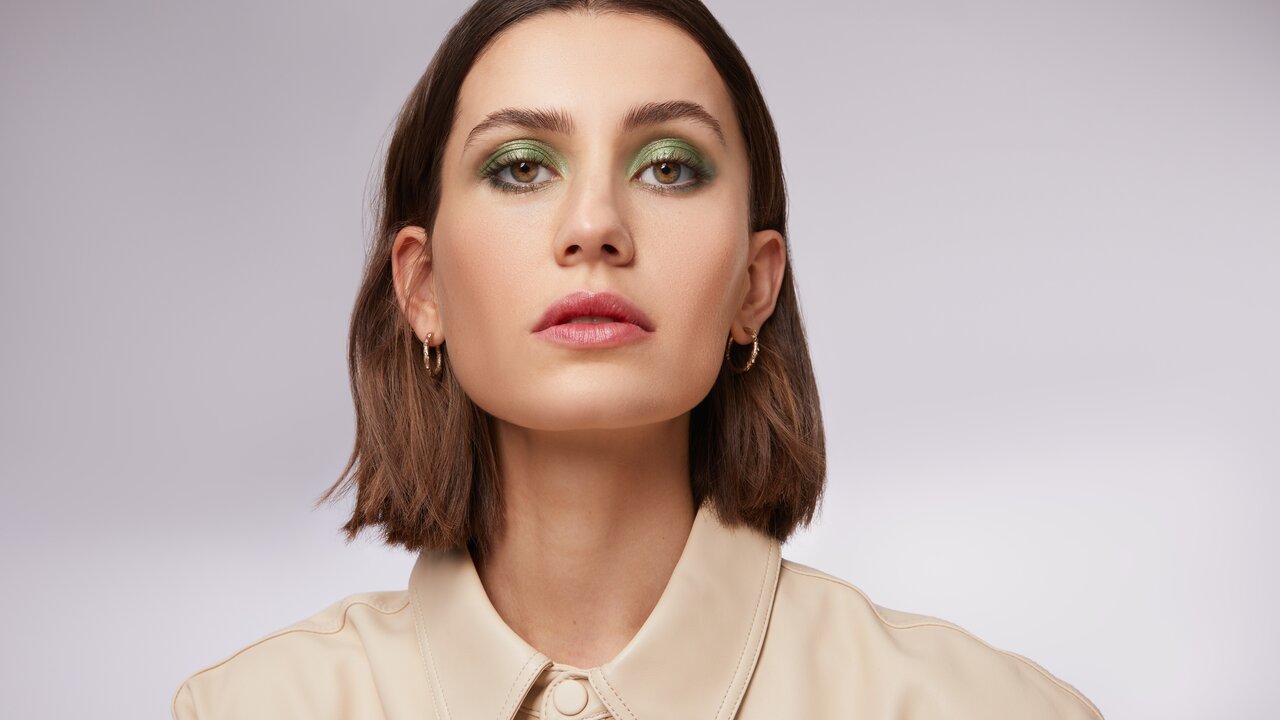 Diese Make-up Trends dürfen Sie nicht verpassen! Portrait einer schönen jungen Frau mit kurzen braunen Haaren und stark geschminkten Augen mit grünem Lidschatten und Metallic Effekt als Sinnbild für die Make-up-Trends im Herbst Winter 2023