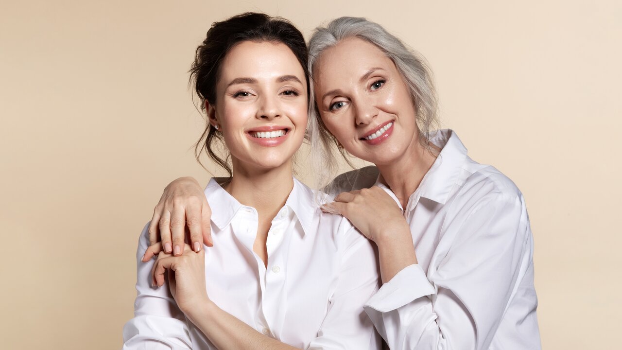 Halbportrait zweier Frauen in dezenten weißen Blusen mit strahlendem Lächeln und rosigem Teint dank dezentem Rouge-Auftrag